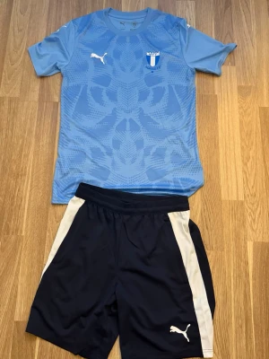 MFF matchställ Puma ljusblå/svart - Säljer ett Malmö FF matchställ från Puma. Tröjan är ljusblå med mönster och klubbmärke på bröstet, samt vit Puma-logga. Shortsen är svarta med vita detaljer och Puma-logga. Perfekt för fotbollsträning eller match!