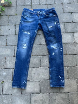 Blå slitna Dondup jeans med raka ben - Säljer ett par blå jeans med slitningar och distressed detaljer på både fram- och baksida. Jeansen har raka ben och klassisk femficksmodell. Perfekta för dig som gillar en avslappnad och trendig stil.