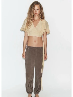 Beige omlottopp med volang - Trendig beige omlottopp med korta ärmar och volangdetaljer. Toppen är croppad och har knytband i sidan för en snygg passform. Perfekt för dig som gillar en lätt och luftig stil till sommaren. Storlek xs. Med lappen kvar