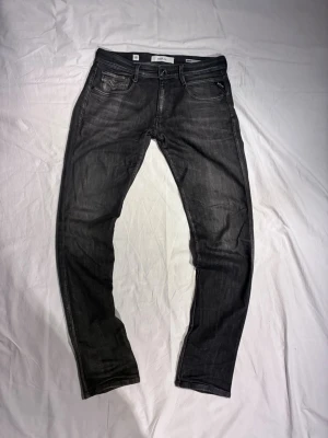 Replay Anbass - Snygga svarta slim fit jeans från Replay med klassisk femficksdesign och diskreta slitningar. Jeansen har dragkedjegylf och Replay-logga på myntfickan. Perfekta för en trendig och avslappnad stil. Jeansen har hål, vilket ska repareras innan köp. Meddela före så får ni se bild på resultatet av reparationen.               Storlek: W31/L34 | Skick: 10/10 förutom ett litet hål som syns på sista bilden. 