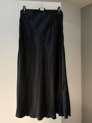 Svart långkjol i satin -  Kjolen är i storlek M, har man storlek M så sitter den lite mer tjat ( som den ”egentligen ska ”  Men jag själv som xs/S har haft den utan några problem, för en mer baggy look . Stilren svart långkjol i glansigt satinmaterial. Kjolen har en mjuk, följsam passform och faller snyggt längs benen. Perfekt att styla med både sneakers och boots för en trendig look.