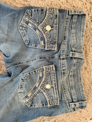 Blå jeans med broderade bakfickor - Snygga ljusblå jeans med unika broderade detaljer på bakfickorna och dekorativa knappar. Klassisk femficksmodell med bälteshällor och dragkedjegylf. Jeansen har en tvättad look och är gjorda i mjukt denimtyg. Från Gina tricot i storlek 158. 