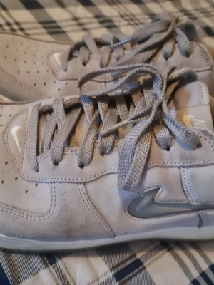 Grå Nike sneakers i mocka - Snygga grå sneakers från Nike i mjuk mocka med klassisk låg siluett. Skorna har perforerad tå, matchande grå skosnören och den ikoniska Nike Swoosh-loggan i silver på sidan. Perfekta för dig som gillar stilrena och bekväma sneakers.