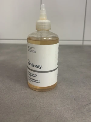 The Ordinary Glycolic Acid Toner - The Ordinary Glycolic Acid 7% Toning Solution i en genomskinlig plastflaska med vit etikett och skruvkork. Tonern är ljusgul och används för att exfoliera huden och ge lyster. Flaskan har en praktisk pipett för enkel applicering.