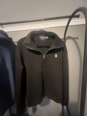 Svart halvzip från Polo Ralph Lauren - Svart tröja med halv dragkedja från Polo Ralph Lauren. Custom fit-modell med klassisk vit logga broderad på bröstet. Mjuk bomullskvalitet och hög krage som ger en clean och stilren look.