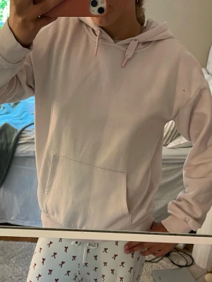 Ljusrosa hoodie med ficka - En enkel och clean ljusrosa hoodie med huva och dragsnören. Hoodien har en stor magficka och ribbade muddar vid ärmar och nederkant. Perfekt för chill dagar eller när du vill ha en avslappnad stil. Materialet känns mjukt och bekvämt. Orginal pris 347kr
