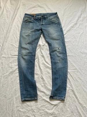 Ljusblå Dondup jeans - Säljer ett par ljusblå jeans med raka ben och slitningar på både lår och knän. Jeansen har klassisk femficksmodell och knappgylf. Perfekta för en avslappnad och trendig look. Slitningarna gör byxorna unika och ovanliga men fortfarande väldigt stilrena.