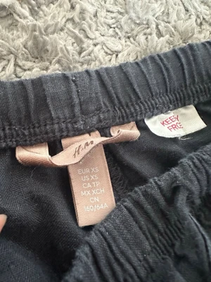 Mörkblåa linnebyxor från H&M  - Säljer ett par mörkblåa linnebyxor från H&M i storlek XS. Byxorna har resår i midjan och dragsko för skön passform. De är vida i modellen och gjorda i ett tunt, luftigt linnematerial som passar perfekt till sommaren.