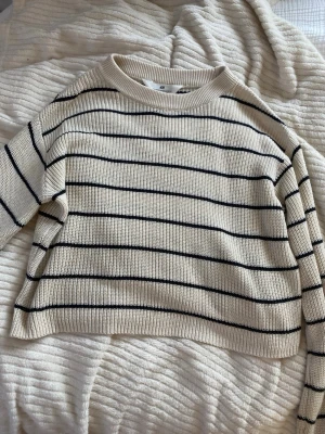 Randig stickad tröja från H&M - Säljer en beige stickad tröja från H&M med svarta horisontella ränder. Tröjan har rund halsringning och långa ärmar. Materialet är mjukt och ribbstickat, perfekt för en avslappnad och trendig look.