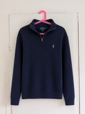 Polo Ralph Lauren marinblå Half Zip 🐎 - Klassisk marinblå half zip/quarter zip från Polo Ralph Lauren. Stilren modell med hög krage, dragkedja och den ikoniska broderade pony-loggan på bröstet. Väldigt lätt att matcha och perfekt för en klassisk/preppy stil. Passar bra till både jeans och chinos. Storlek: M (10-12) Skick: Fint skick men den har en fläck/missfärgning! Skriv gärna om du vill ha mått eller fler bilder!