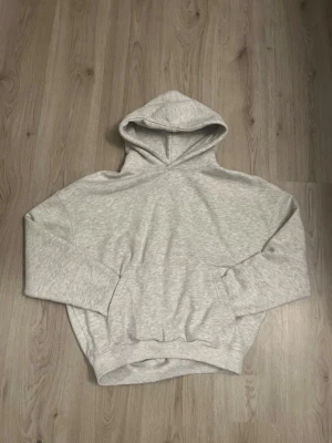 Ljusgrå hoodie från Pull&Bear - En stilren ljusgrå hoodie från Pull&Bear med klassisk huva och magficka. Tillverkad i mjukt material som känns skönt mot huden. Perfekt för dig som gillar en enkel och clean look. Passar till det mesta och är lätt att matcha med andra plagg.