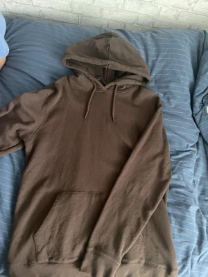 Brun hoodie från 157 - Säljer en enkel och stilren brun hoodie från 157 med huva och dragsnören. Hoodien har en stor magficka och ribbade muddar vid ärmslut och nederkant. Perfekt för chill dagar eller när du vill ha en avslappnad look.