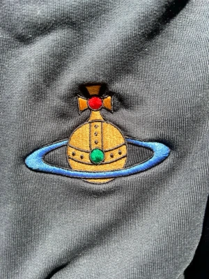 Mörkblå sweatshirt med broderad logga - Mörkblå sweatshirt med ikonisk broderad logga i gult, blått, rött och grönt på bröstet. Tröjan har rund halsringning, långa ärmar och ribbade muddar vid ärmslut och nederkant. Perfekt för en avslappnad och trendig stil.
