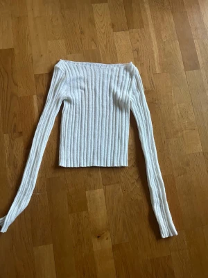 Vit ribbstickad långärmad tröja - Säljer en vit ribbstickad tröja med lång ärm och rak passform. Tröjan är tajt, något båtformad halsringning och är tillverkad i ett mjukt stickat material. Perfekt för lager-på-lager och enkel att matcha med olika outfits.