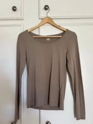 Beige långärmad topp - En enkel och stilren beige långärmad topp med rund halsringning. Tillverkad i ett mjukt och stretchigt material som sitter skönt på kroppen. Perfekt att matcha med jeans eller kjol för en clean look.
