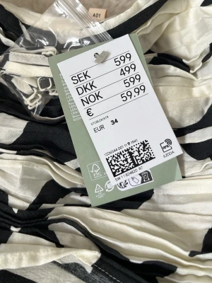 Vit och svart blommig klänning - Säljer en snygg vit klänning med stora svarta blommor. Klänningen har en axelbandslös design och ett omlottliknande liv. Perfekt för dig som vill sticka ut med ett coolt mönster och en feminin siluett. Aldrig använd - nypris är 600 kr! Storlek 34/XS men funkar för både 32 & 36.