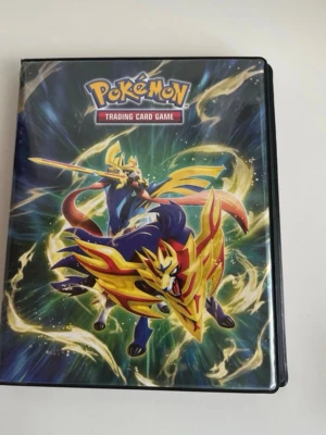 Pokémon samlarpärm med kort - Säljer en Pokémon samlarpärm med färgglatt omslag och illustration av Zacian. Inuti finns plastfickor med flera Pokémonkort, bland annat Pikachu V och Riolu. Perfekt för dig som vill organisera och visa upp din samling av Pokémonkort. Tyska kort visas på bilden