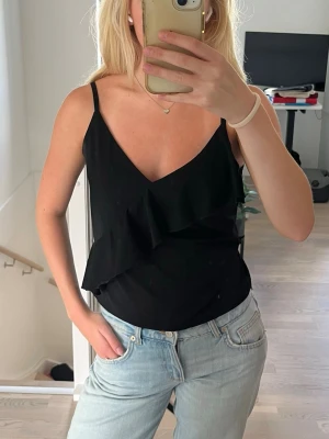 Svart linnetopp med volang - Snygg svart topp med volanger! Storleken upplevs mindre än normalt skulle jag vilja säga.