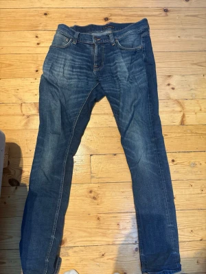 Blå slim fit jeans med slitningar - Snygga blå jeans i slim fit-modell med klassiska fem fickor och coola slitningar framtill. Jeansen har en lätt tvättad look och kontrastsömmar. Perfekta för en avslappnad och trendig stil.
