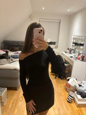 Svart oneshoulder topp - Snygg svart topp med oneshoulder-design och långa ärmar. Toppen har en tight passform som framhäver figuren och en stilren look. Perfekt för dig som gillar minimalistisk och trendig stil.