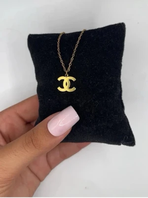 Guldigt halsband med CC-hänge - Snyggt halsband i guldfärg med ett klassiskt CC-hänge. Kedjan är tunn och elegant, och hänget har en blank finish som ger en lyxig känsla. Perfekt accessoar för att lyfta vilken outfit som helst.