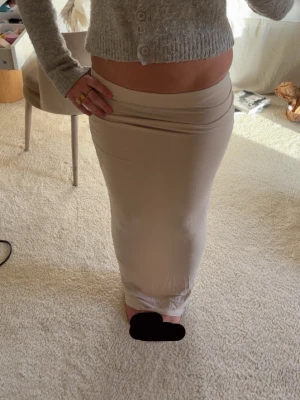 Beige lång tight kjol - Säljer en beige långkjol med tight passform. Kjolen har en enkel och stilren design utan synliga detaljer eller mönster. Perfekt för dig som gillar minimalistisk stil och vill ha en kjol som är lätt att matcha med olika toppar.