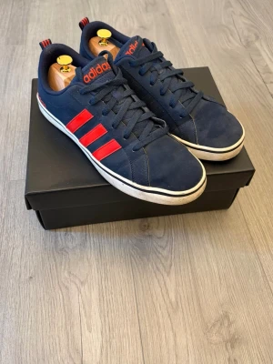 Marinblå Adidas sneakers med röda detaljer - Snygga marinblå sneakers från Adidas👟 Skorna är i modellen DAILY. Skorna är i ett mycket bra skick!✅ Skornar i storlek 44📐 Skriv vid funderingar!✅ Postar inom 24h🚚📦!