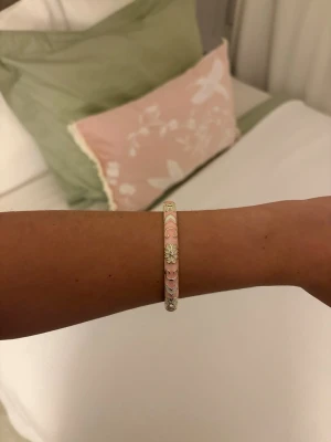Pastellfärgat armband med blommor - Säljer ett superfint armband i pastellfärger med blommönster och pärldetaljer. Armbandet har en rund form och går i rosa, vitt och grönt. Perfekt accessoar för att piffa upp din outfit med en söt och lekfull touch.