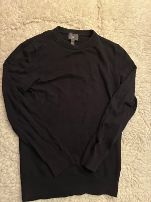 Svart stickad tröja från H&M - En enkel och stilren svart stickad tröja från H&M. Tröjan har rund halsringning, långa ärmar och ribbade muddar vid ärmslut och nederkant. Perfekt basplagg till garderoben och lätt att matcha med olika outfits.