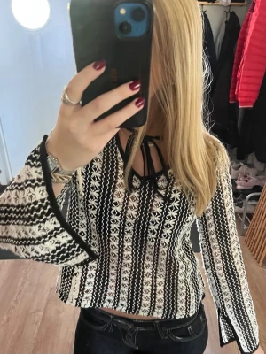 Mönstrad stickad tröja med vida ärmar - Säljer en snygg stickad tröja med svartvitt mönster och vida ärmar. Blusen har knytning vid halsen och är croppad i modellen.💕