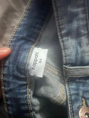 Blå jeans från Kappahl, storlek 164 - Säljer ett par klassiska blå jeans från Kappahl i storlek 164. Jeansen har två bakfickor, hällor för skärp och är sydda i mjukt denimtyg med gul kontrastsöm. Perfekta för en avslappnad och stilren look.