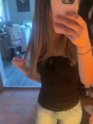 Svart ribbad ärmlös topp med knyt - Säljer en svart ribbad topp med knyt framtill. Toppen är ärmlös och har en figurnära passform som framhäver siluetten. Perfekt att matcha med jeans eller kjol för en trendig look.