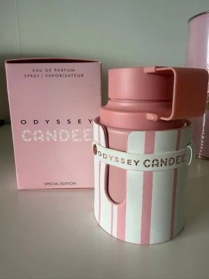 Odyssey Candee Eau de Parfum, 100 ml - Helt ny, köpt på Noriloo.Odyssey Candee Eau de Parfum Special Edition med en unik rosa och vit randig flaska i plast och metall. Flaskan har ett modernt, cylinderformat utseende med ett praktiskt lock och matchande rosa förpackning. Doften är feminin och trendig.