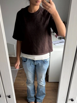 Mörkbrun stickad tröja med kort ärm - En mörkbrun stickad tröja med boxig passform och korta ärmar. Tröjan har rund halsringning med ribbstickad kant och är tillverkad i ett mjukt material. Perfekt att styla över en långärmad topp eller t-shirt.