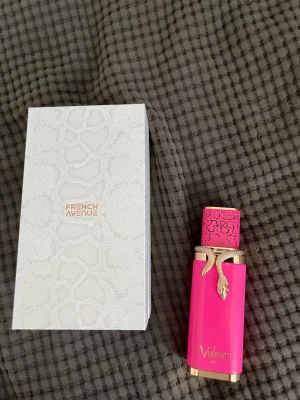 Vulcan baie parfym från French Avenue - Snygg parfymflaska i starkt rosa med gulddetaljer och ett unikt ormformat lock. Flaskan har texten 'Vulkan' och kommer i en elegant vit kartong med ormmönster. Perfekt för dig som gillar lyxig och iögonfallande design. 99 procent kvar.