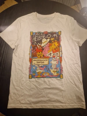 Vit T-shirt Håkan Hellström Sommarturné - Vit T-shirt med färgglatt tryck på bröstet från Håkan Hellströms sommarturné 2026. Trycket har tecknade figurer, noter och text. Klassisk rund hals och korta ärmar. Perfekt för dig som gillar musik och vill sticka ut med en unik konserttröja.