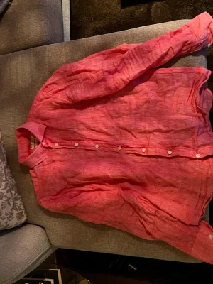 Rosa linneskjorta från Blue Coast - Säljer en snygg rosa skjorta från Blue Coast i relaxed regular fit. Skjortan är tillverkad i linne, har klassisk krage, långa ärmar och vita knappar framtill. Perfekt för dig som vill ha en luftig och stilren skjorta till sommaren. Lite skrynklig bara men enkelt löst 