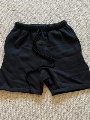Essentials shorts - Ett par svarta essentials shorts med svart text nere vid vänstra benet. De är i storlek S och i nytt skick. Pris kan diskuteras och skriv om du har några frågor. 