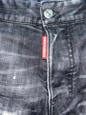 Svarta Dsquared2 Jeans - Säljer ett par svarta Dsquared2 jeans med coola slitningar och färgstänk. Jeansen har smal passform och klassisk femficksdesign. Materialet är denim med en tvättad look och detaljer som ger en trendig streetkänsla.