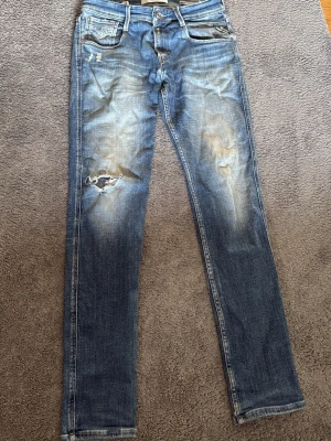 Blå slitna jeans från Replay - Säljer ett par blå jeans från Replay med slitningar och ett hål i knät som jag råka riva sönder med de går att sy igen. De va en lite slitning från början som de ska vara men sen råka de gå sönder. Går att laga, de är i bra skick annars.