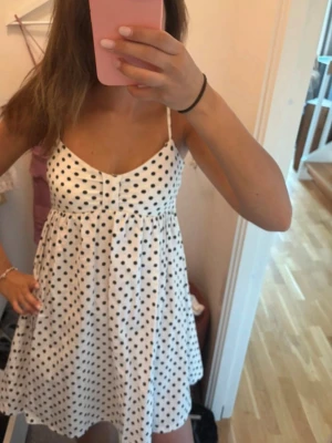  Ny populärt Vit prickig kort sommarklänning S/M - Söt vit klänning med svarta prickar och tunna axelband. Klänningen har en lätt utställd passform och är kort i modellen, perfekt för varma dagar. Materialet känns lätt och luftigt, vilket gör den skön att bära under sommaren.