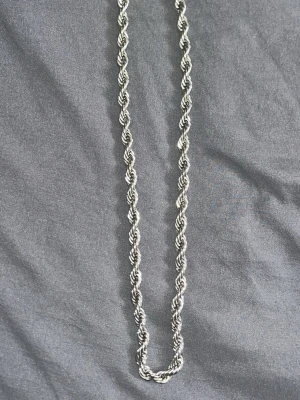 Silverfärgat tvinnat halsband - Snyggt halsband i silverfärg med tvinnad kedja som ger en chunky och modern look. Halsbandet har en metallisk glans och passar perfekt för dig som gillar stilrena accessoarer med lite edge. Materialet ser ut att vara metall och designen är enkel men ändå iögonfallande.
