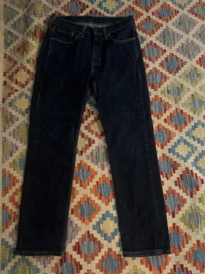 Mörkblå straight jeans från Levi's - Snygga mörkblå jeans från Levi's med klassisk rak passform och fem fickor. Jeansen har kontrastsömmar och en ikonisk läderpatch bak i midjan. Tillverkade i slitstark denim som ger en tidlös look. Storlek 30/30