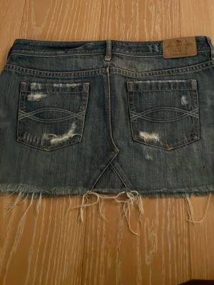 Kort jeanskjol med slitningar - Säljer en kort, blå jeanskjol från abercrombie & fitch i storlek M (EU40)
