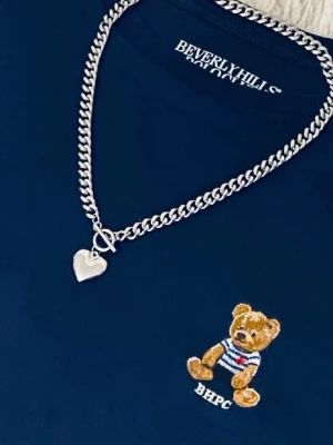 Silverfärgat halsband med hjärthänge - Snyggt halsband i silverfärg med en kraftig kedja och ett hjärtformat hänge. Halsbandet har en modern och stilren design som passar till många olika looks. Perfekt accessoar för att lyfta din outfit.