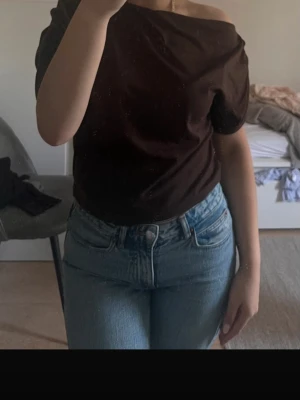 Mörkbrun offshoulder topp - Snygg mörkbrun offshoulder topp med korta ärmar och avslappnad passform. Perfekt att styla med jeans eller kjol för en trendig look. Tyget ser mjukt och bekvämt ut, och toppen har en enkel men chic design.