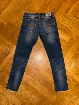 Blå jeans från Nudie Jeans - Snygga blå jeans från Nudie Jeans med klassisk femficksdesign och orangea sömmar på bakfickorna. Jeansen har en rak passform och är tillverkade i denim. Perfekta för en avslappnad och trendig stil. Storlek W31 L30 (36 som är uppsydda till 30!)