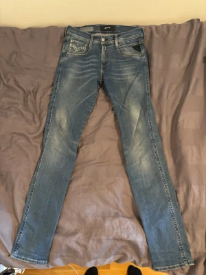 Replay anbass - Säljer ett par blå slim fit jeans med snygga vita kontrastsömmar och klassiska fem fickor. Jeansen har en lätt tvättad look och smala ben. Passar perfekt till en avslappnad stil och är tillverkade i stretchigt denimtyg för extra komfort.
