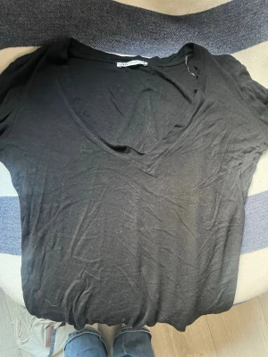 Svart v-ringad t-shirt från Zara - En svart t-shirt från Zara med v-ringning och korta ärmar. Tillverkad i ett mjukt bomullsmaterial som känns skönt mot huden. Enkel och stilren modell som passar till det mesta. Perfekt basplagg för garderoben.