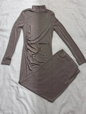 Beige långklänning från SHEIN - Långklänning i beige från SHEIN med polokrage och långa ärmar. Klänningen har en snygg rynkning i sidan som ger en cool detalj och är gjord i ett mjukt, stretchigt material som känns skönt mot huden.